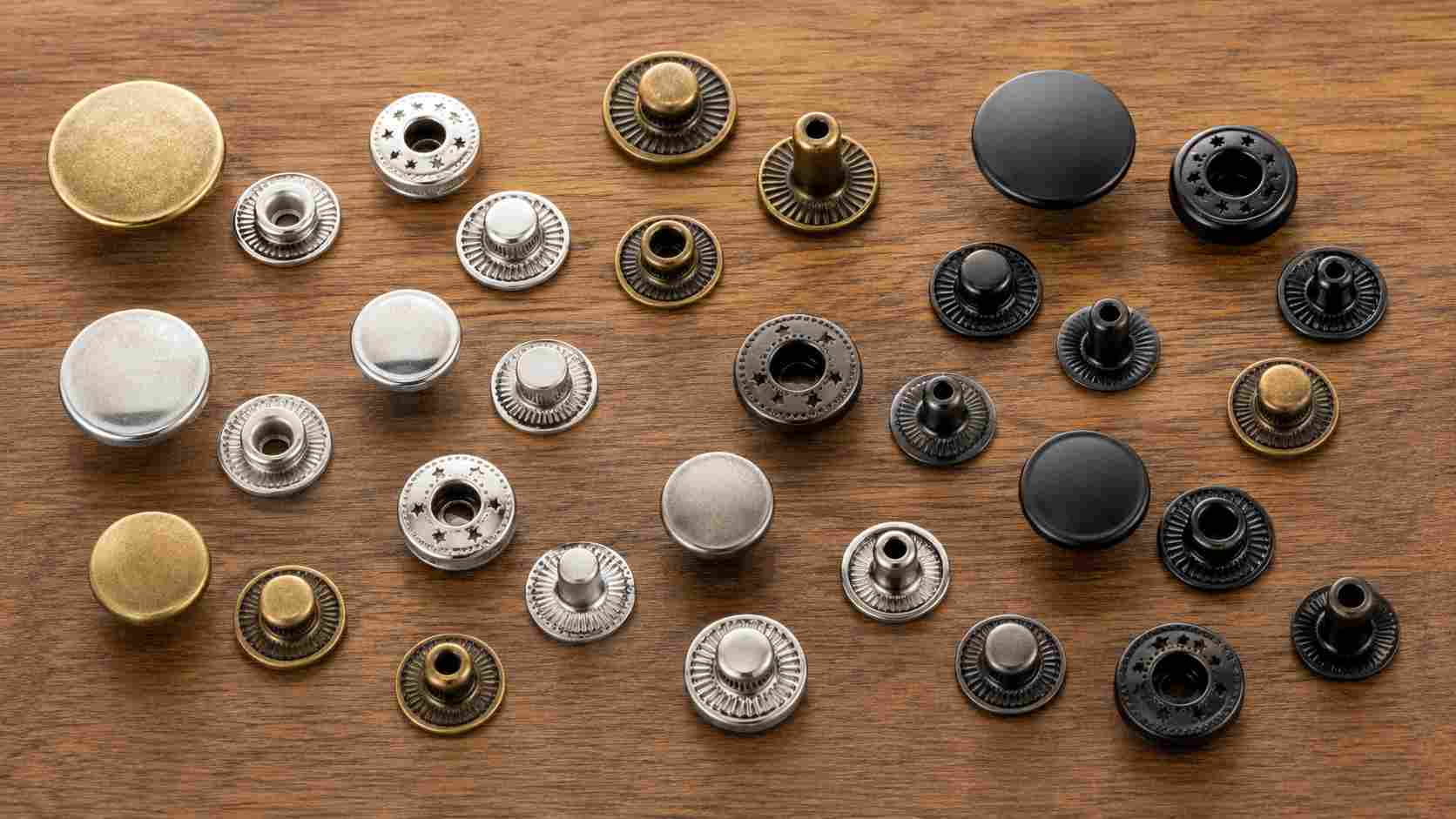 button fasteners, Button fasteners in gold, silver, black, and antique finishes are arranged with their matching components on a wooden surface.